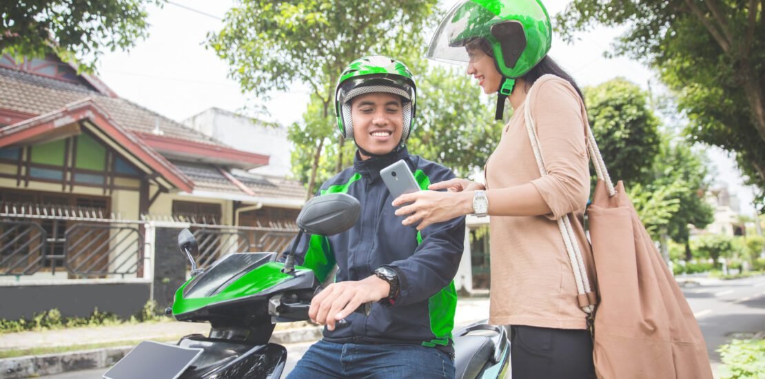 woman standing sidewalk ordering commercial motorcycle taxi scaled